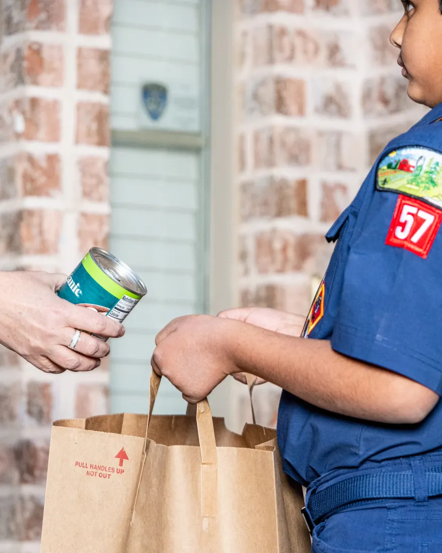 Cub Scout accepting a donated can of food during a Scouting for Food collection